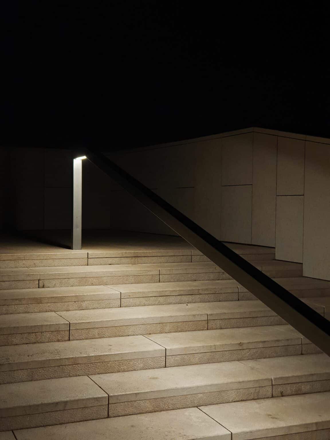Escalier de pierre éclairé de nuit par une borne lumineuse le long d'une rampe, sur fond noir
