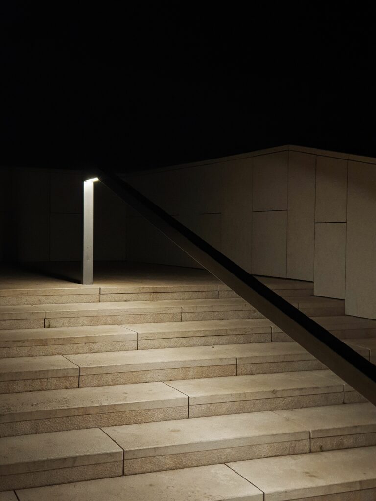 Escalier de pierre éclairé de nuit par une borne lumineuse le long d'une rampe, sur fond noir