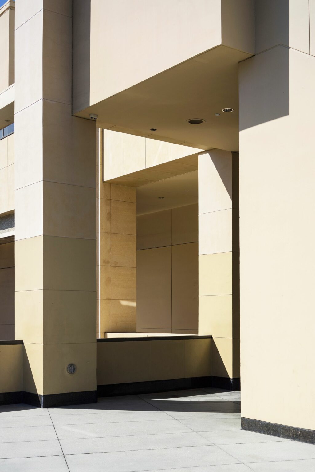 Façade d'immeuble beige aux piliers massifs et jeux d'ombre et de lumière
